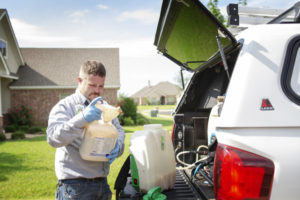 An 855Bugs exterminator is shown at the back of his truck mixing pesticides to treat the exterior of a home for fleas and ticks.