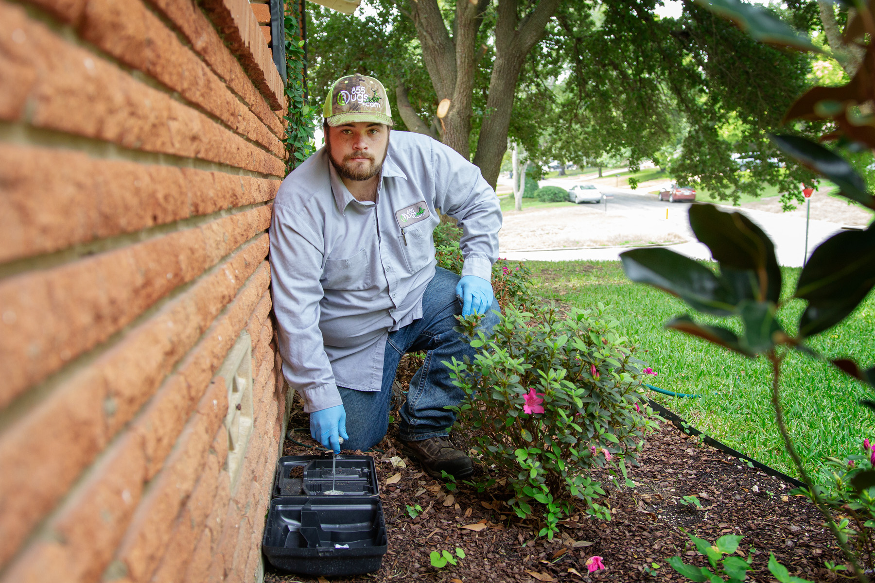 An 855Bugs technician is tending to a bait trap outside a brick home in Waco, Texas.