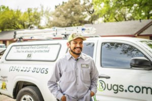 An 855Bugs pest control expert is shown standing in front of his truck with a big smile on his face.