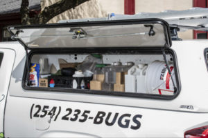 A compartment on the side of an 855Bugs vehicle is open revealing pesticides.