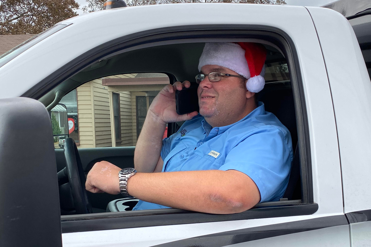 Eric Benson sits in an 855Bugs truck wearing a Santa hat and talking on the phone.