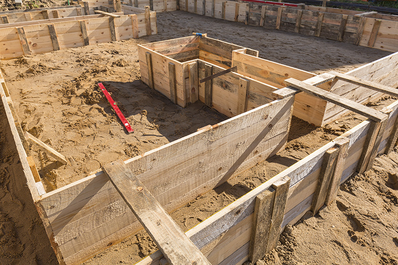 A structure is in the beginning stages of construction with wood framing along the dirt ground.