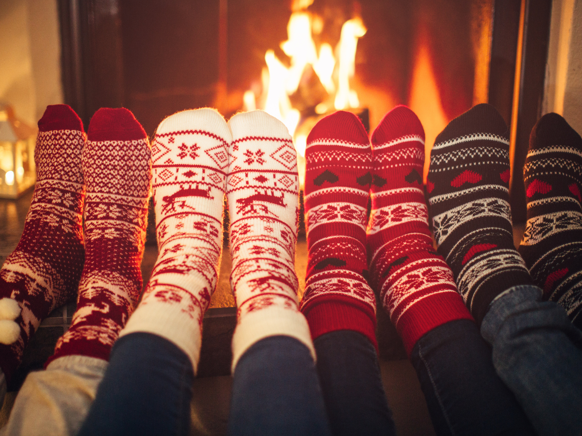 Family warming their feet around the fire featuring colorful socks. Bed Bug Winter Vacation Blog